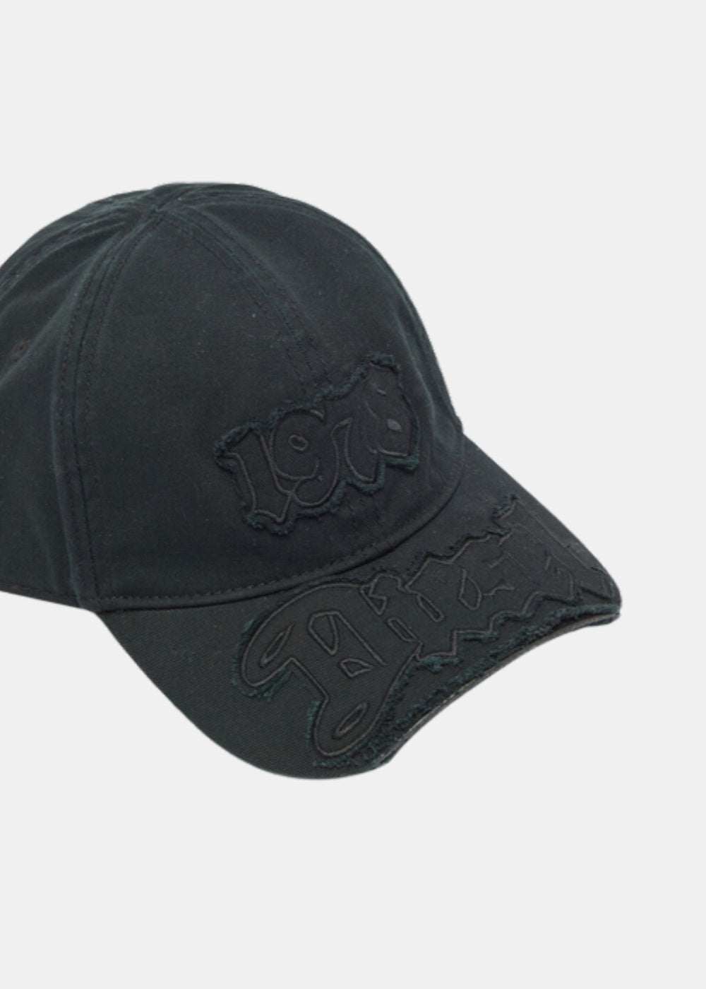 Gros plan sur l'appliqué effiloché et la visière au bord vieilli d'une casquette baseball noire Diesel C-renel en gabardine de coton.