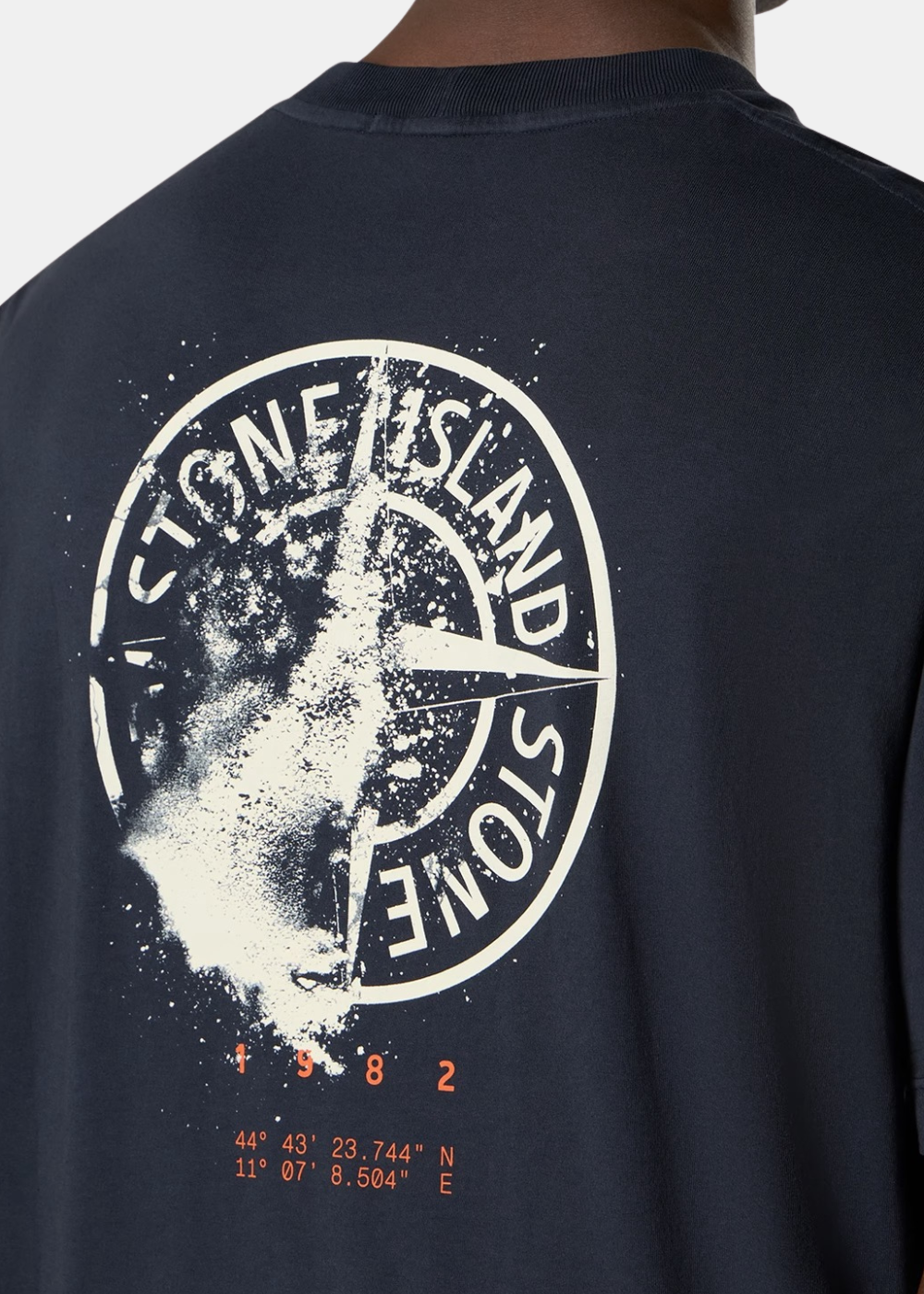 Gros plan sur l'omoplate du t-shirt marine, révélant la texture du tissu et l'effet graphique blanc boussole et orange.