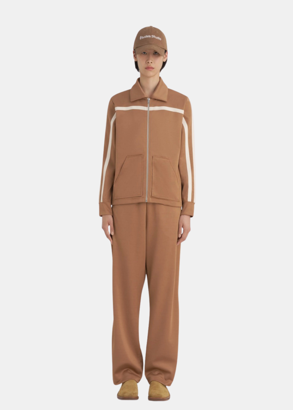 Mannequin femme portant la veste de survêtement Études Studio marron de face avec bandes appliquées sur les manches ainsi que le pantalon du même  style que la veste .