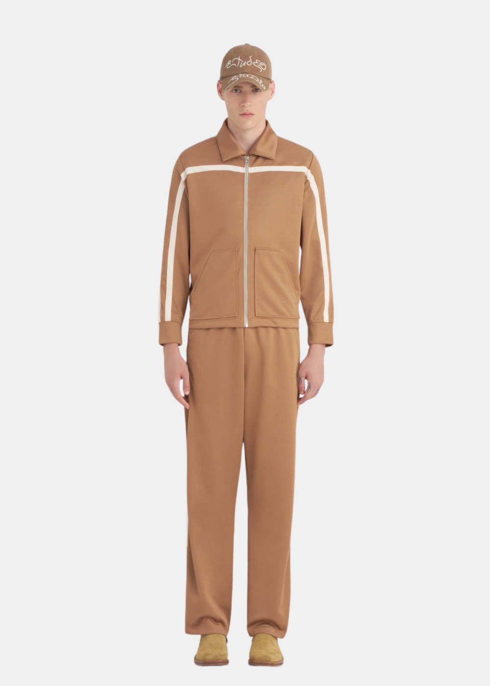 Mannequin homme portant la veste de survêtement Études Studio marron de face avec bandes appliquées sur les manches ainsi que le pantalon du même  style que la veste .