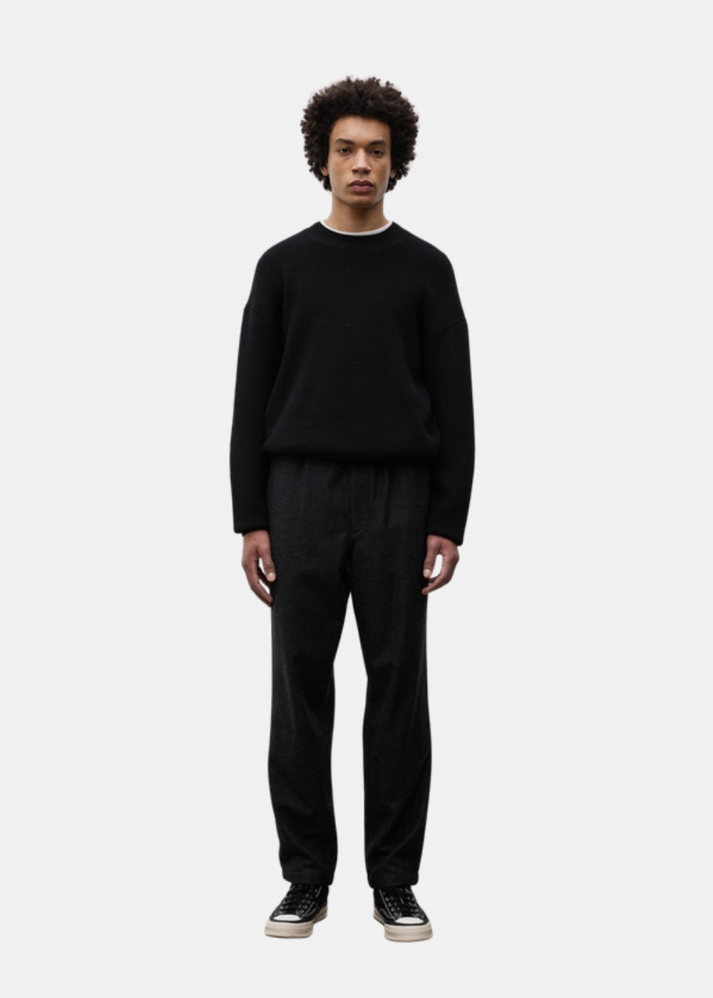 Porté de face en pied d'un pantalon regular gris anthracite Norse Projects Trysil associé à un pull sombre et des baskets noires.