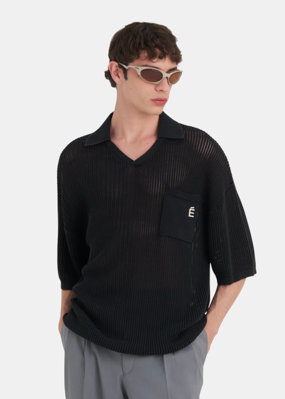 Homme portant le polo en dentelle de coton noir Études Studio, coupe fluide avec transparence et col en V.