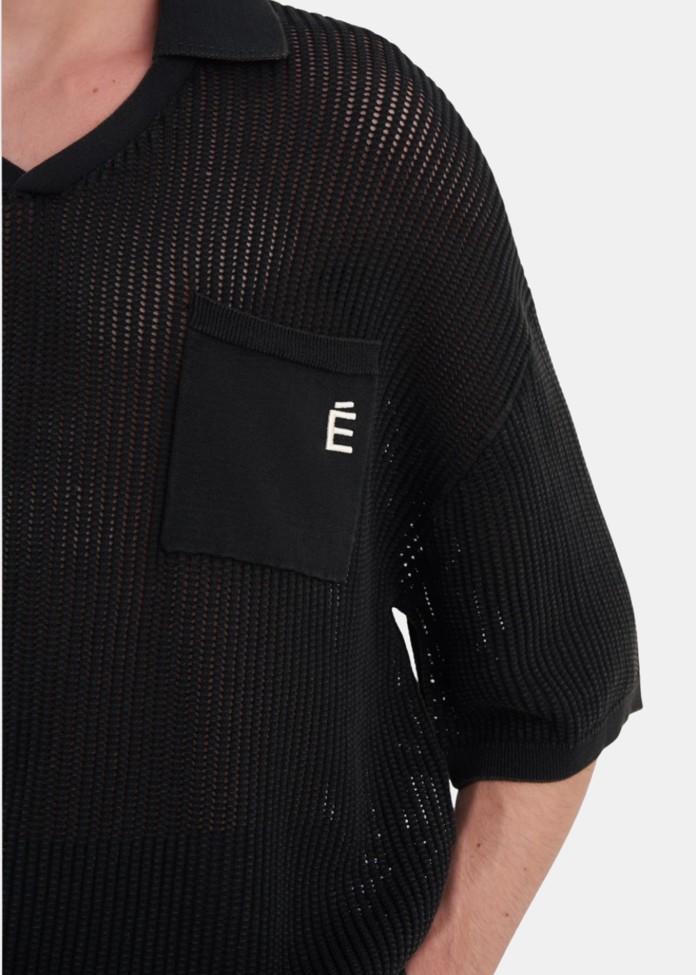 Gros plan sur le patch "É" brodé sur la poche poitrine et la texture ajourée de la dentelle en pur coton.