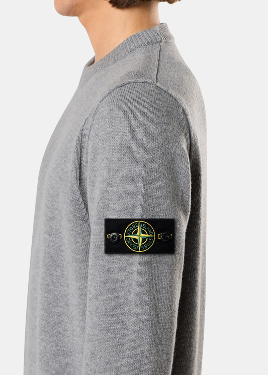 Porté de profil mettant en valeur le badge boussole Stone Island boutonné sur la manche d'un pull en laine gris chiné.
