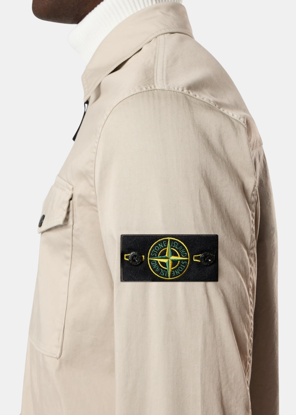 Zoom de profil sur la manche d'une surchemise en satin de coton stretch beige Stone Island avec son célèbre badge boussole.