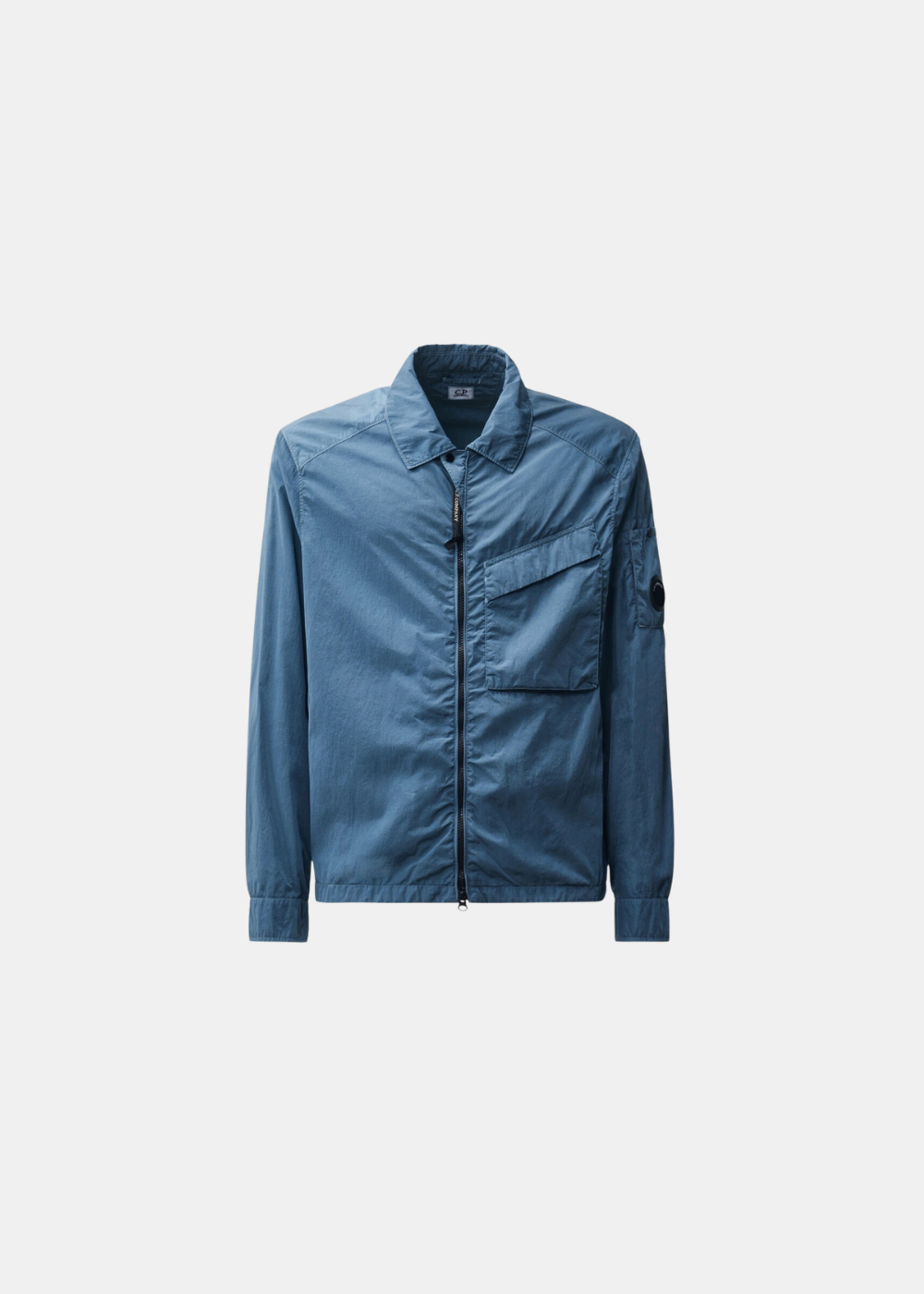 Surchemise technique bleu orion pour homme posée à plat, vue de face, dotée d'un col classique, d'une fermeture zippée, d'une poche poitrine plaquée et du détail de la lentille (Lens) sur la manche gauche.