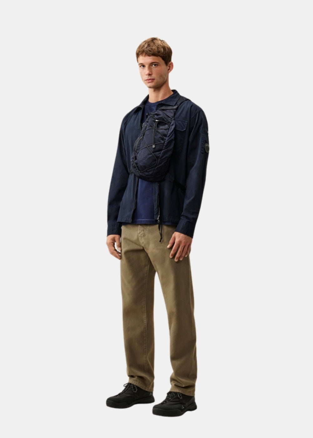 Porté en pied d'une surchemise zippée marine C.P. Company associée à un pantalon kaki et des chaussures sombres, coupe classique.