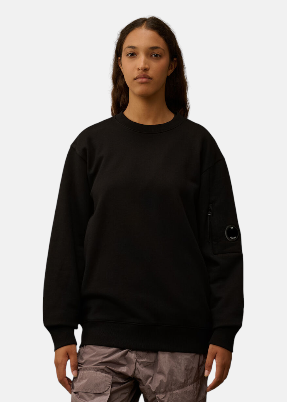 Femme portant le sweat C.P. Company col rond noir, badge lentille sur la manche.