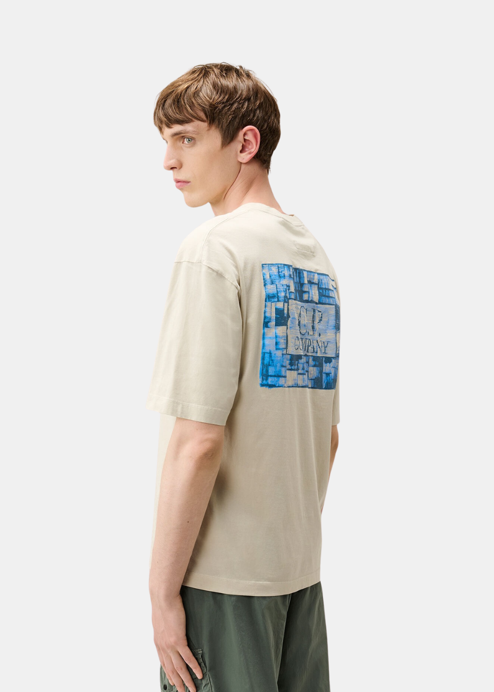 Vue de trois-quarts dos d'un t-shirt beige C.P. Company porté mettant en valeur le grand imprimé logo bleu.