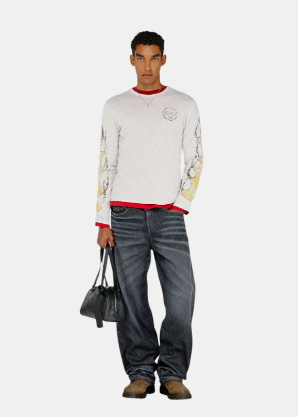 Porté en pied d'un T-shirt manches longues Diesel gris avec jean ample bleu délavé, sac noir à la main et chaussures marron.