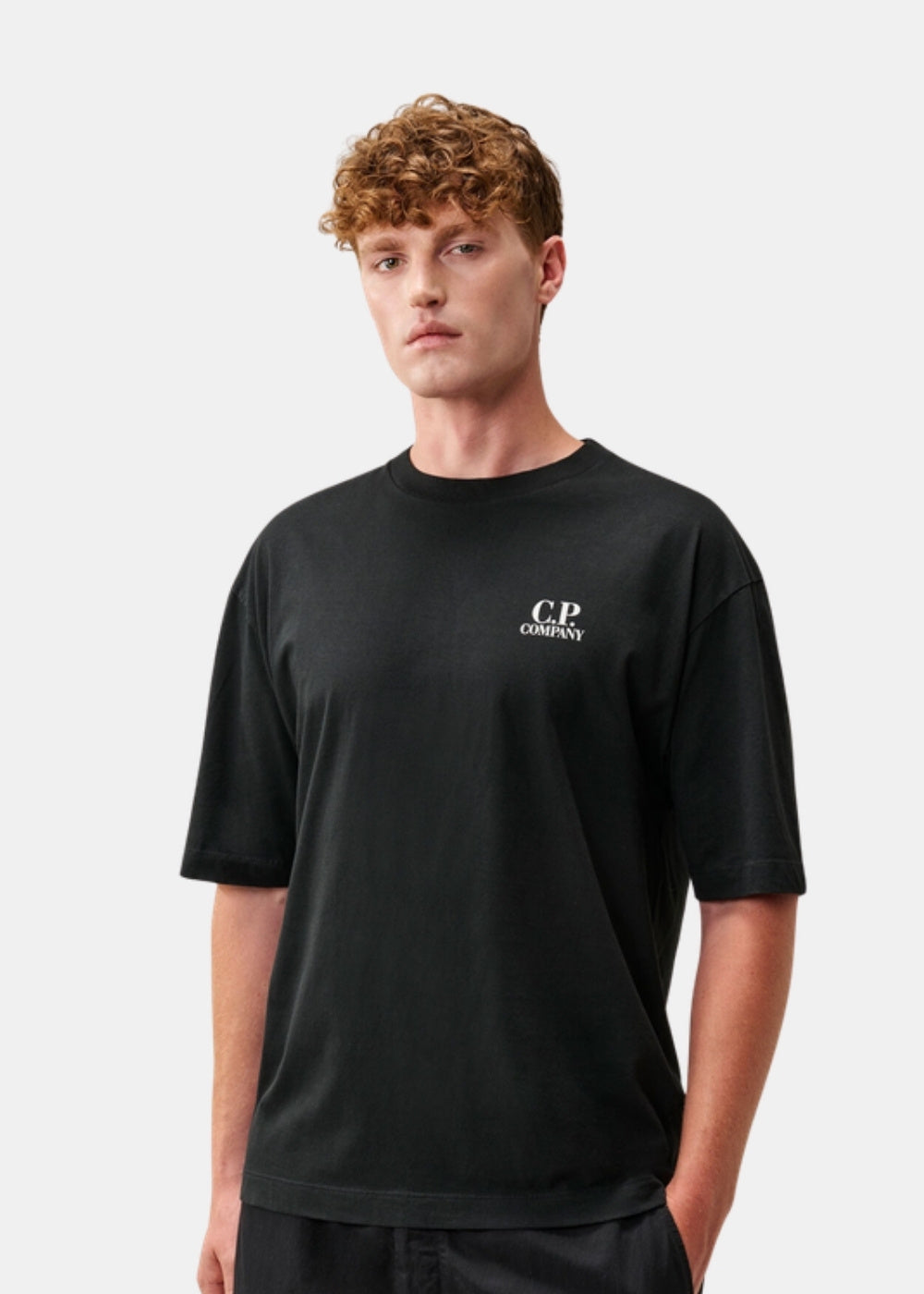 Porté de face d'un t-shirt noir C.P. Company à manches courtes, col rond côtelé et logo imprimé sur la poitrine, coupe confort.