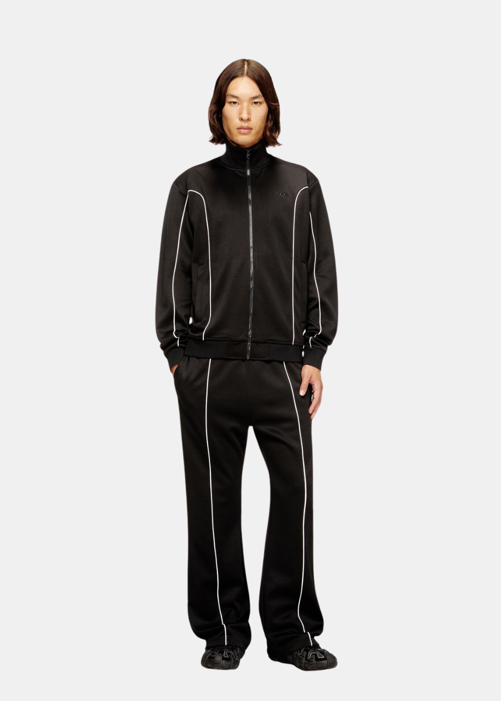 Silhouette complète du mannequin portant l'ensemble de survêtement Diesel noir assorti avec liserés blancs et baskets sombres.