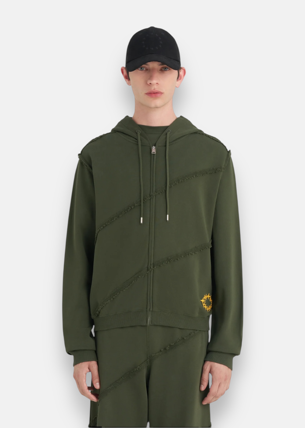 vue de face du mannequin portant le Sweat à capuche Zippé Études Studio vert forêt avec son pantalon assortie. cette photo mets en avant les détails de broderie du sweat études